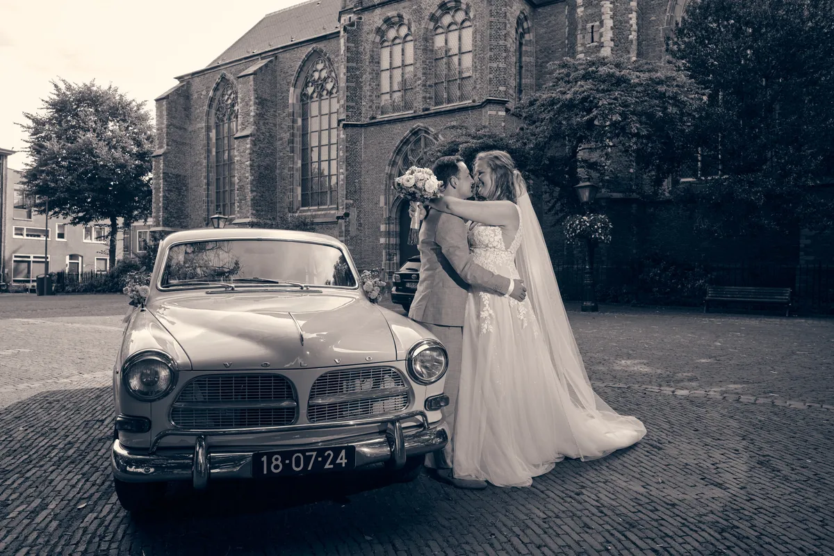 Zwart-wit: Julia en Rens kussen naast de Volvo Amazon met het kenteken van hun trouwdatum