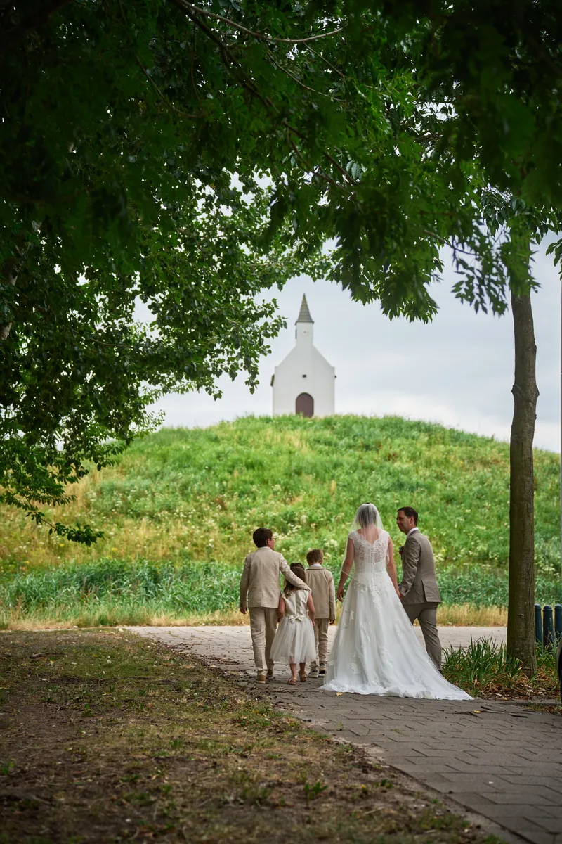 Rutger, Caroline en de kinderen lopen over het pad naar het witte kerkje op de terp