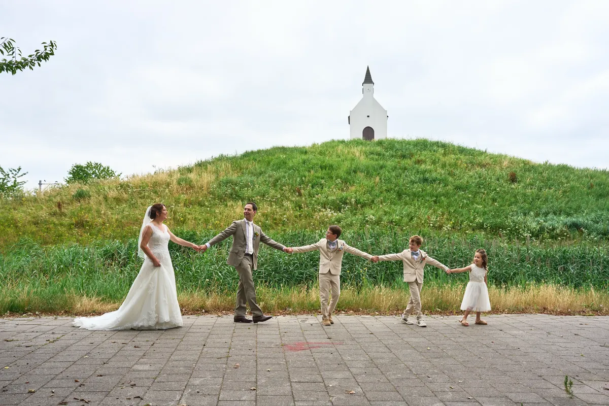 Het gezin staat hand in hand op een rij, met het kerkje op de heuvel erachter