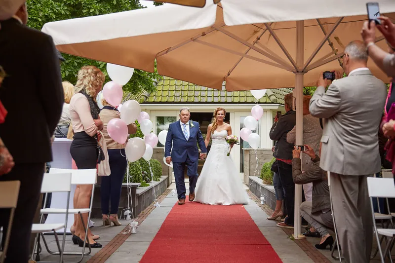 Trudy loopt over de rode loper onder de parasols naar voren