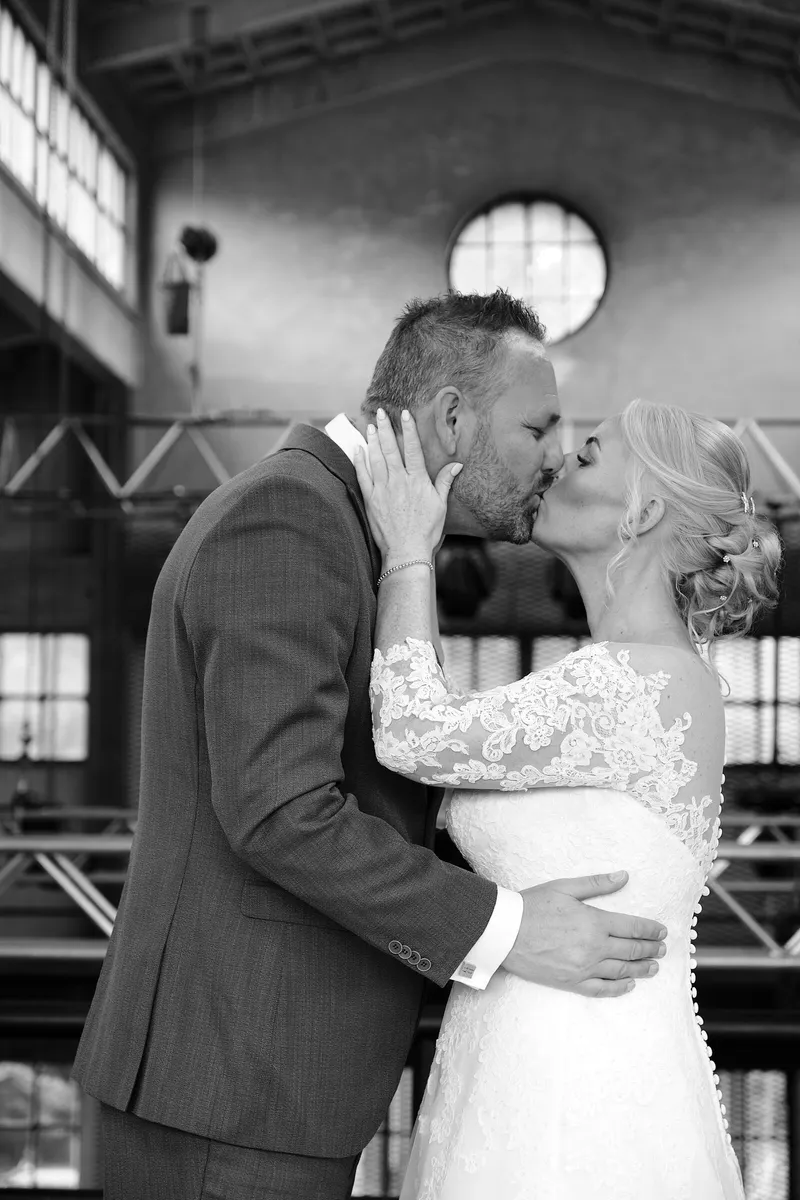 Marleen en Eric kussen in de hal met het ronde raam, zwart-wit