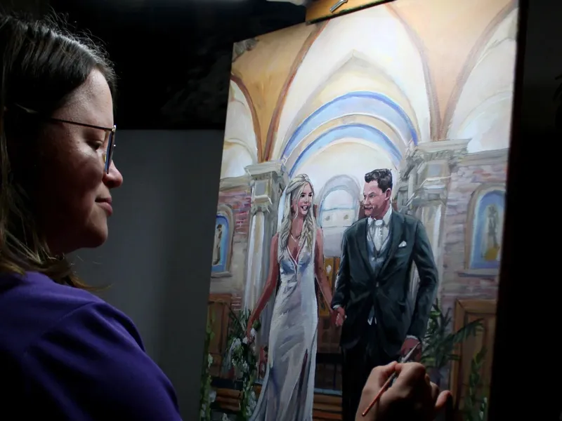 Een live schilderes met penseel bij haar ezel, met een schilderij van een bruidspaar in een kerk