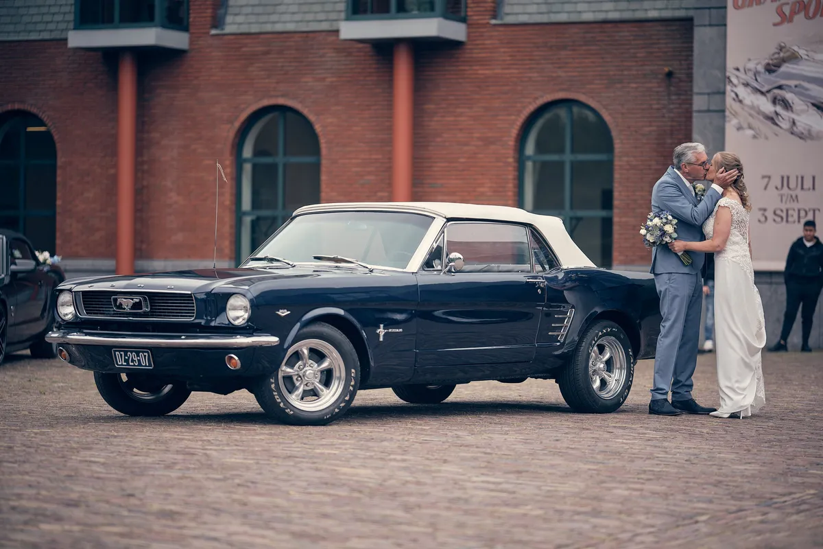 De Mustang-cabrio met Ingeborg en Herre voor de bakstenen gevel van het Louwman Museum