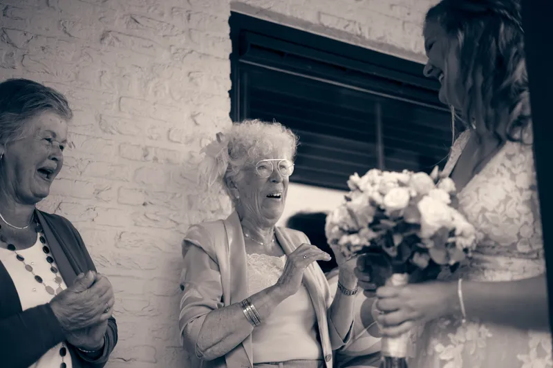 Zwart-wit: twee oudere vrouwen lachen naast Julia met haar boeket