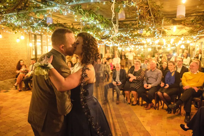 Maurice en Chantal kussen onder de lichtjes in de serre van Vlietzicht, de gasten kijken toe