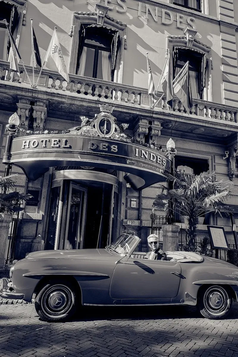 Zwart-wit: de bruidegom rijdt in een klassieke Mercedes-roadster voor bij Hotel des Indes om zijn bruid op te halen