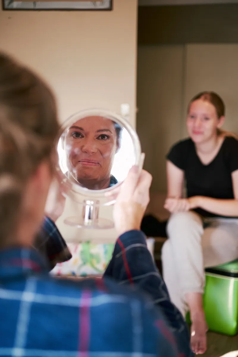 Mirjam bekijkt haar make-up in een spiegeltje, haar dochter kijkt toe