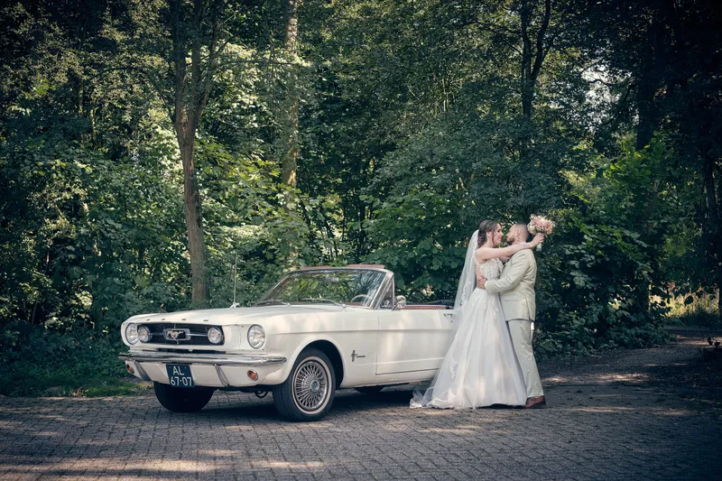 Wendy en Robin kussen naast de witte Mustang op een laan