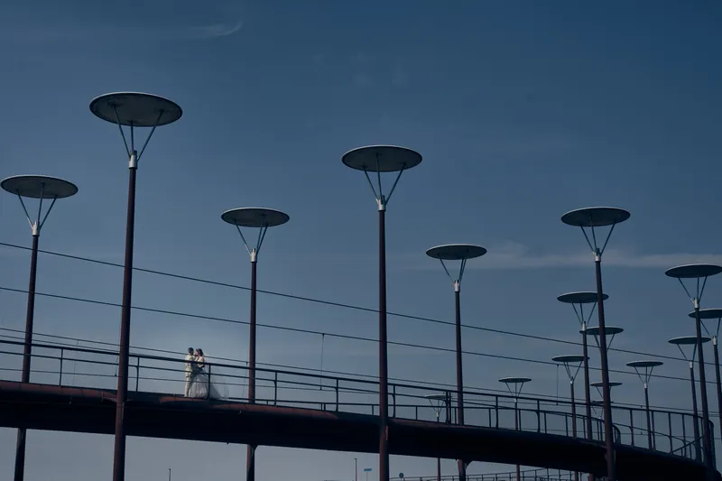 Wendy en Robin klein op een brug met hoge lantaarnpalen, tegen een blauwe lucht