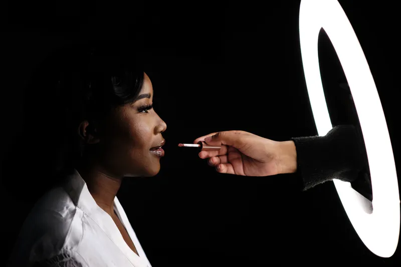 Natascha in het donker, een hand met een kwastje komt door de ringlamp het beeld in