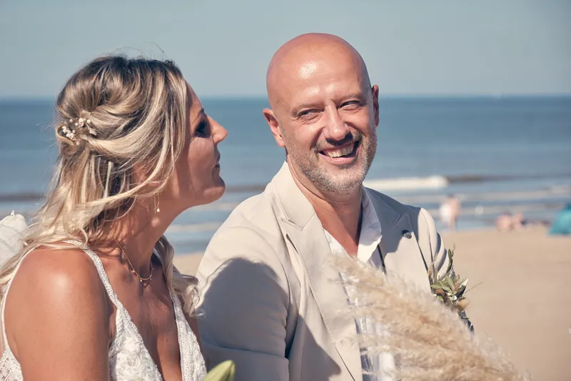 Jolanda en Pascal lachen tijdens de ceremonie, met de zee erachter