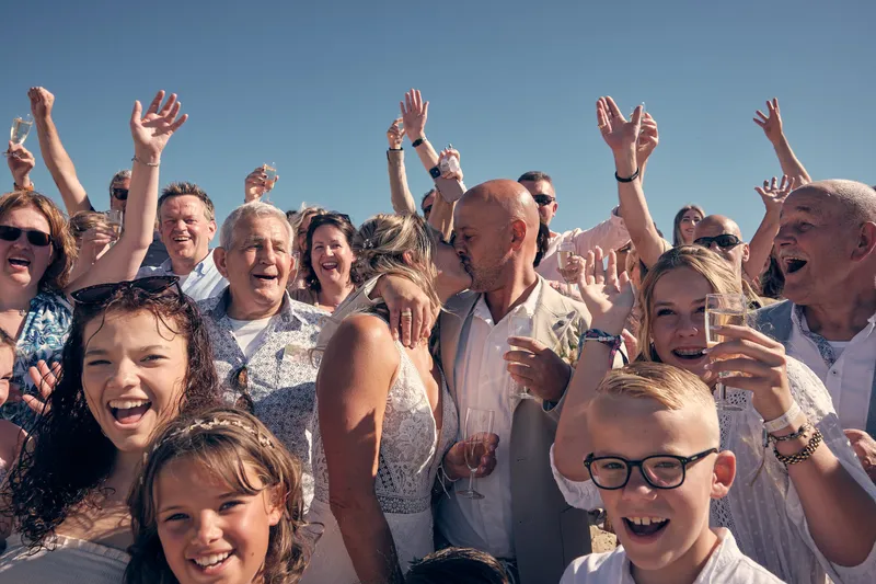 De gasten juichen bij de groepsfoto op het strand