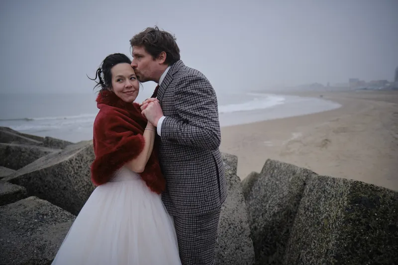 Niels kust Margueritte op de stenen in de koude mist boven het strand van Scheveningen