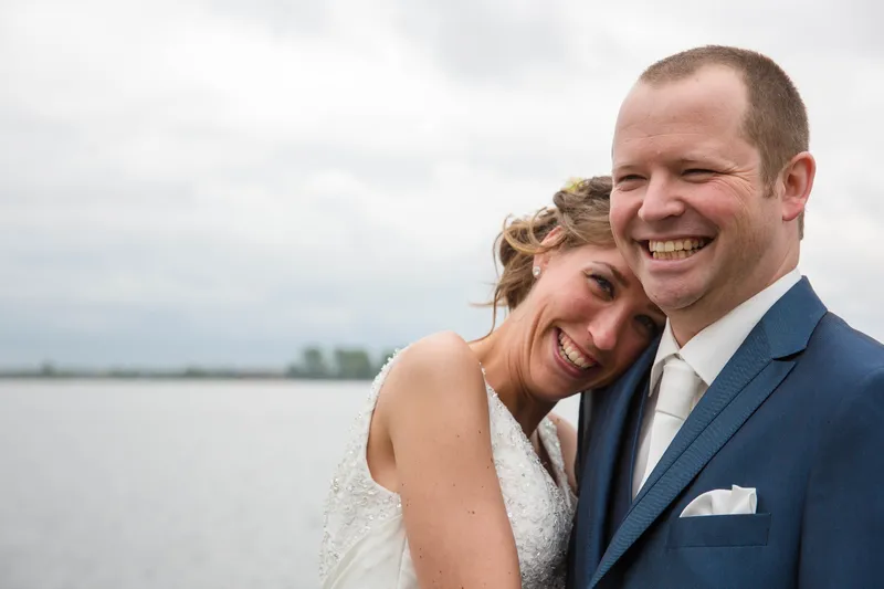 Elise leunt lachend tegen Maarten, met het water op de achtergrond