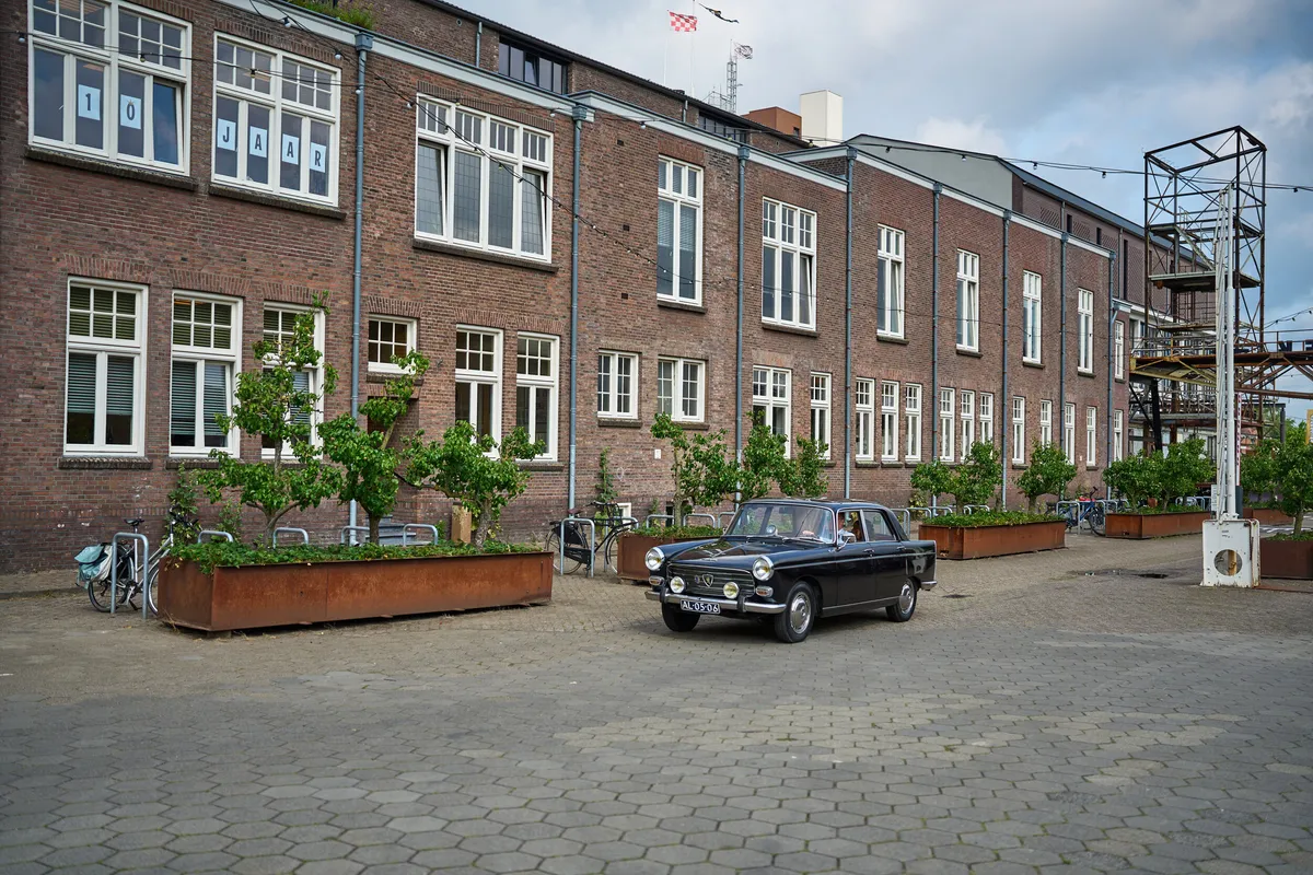 Het bakstenen fabrieksgebouw van De Noordkade, met een zwarte oldtimer op het plein
