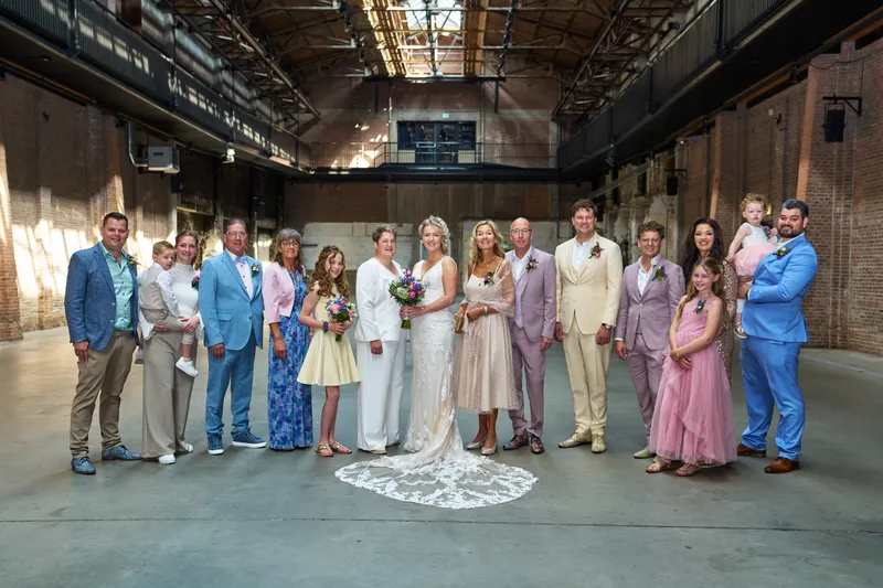De familie staat samen met de bruiden midden in de hal, onder de stalen spanten