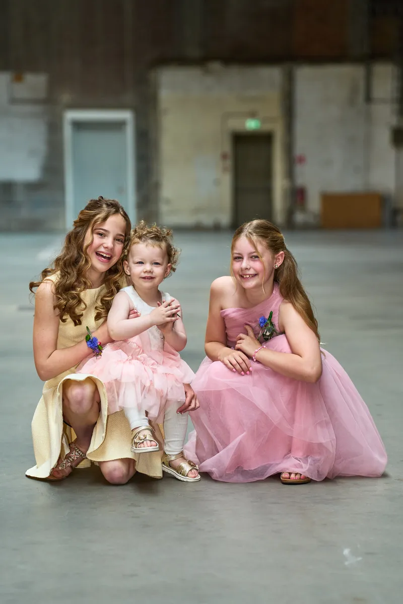 De bruidsmeisjes in roze en gele jurkjes op de vloer van de hal