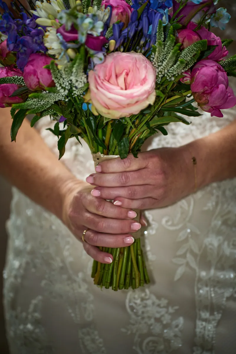 Het boeket met een roze roos en paarse bloemen in de handen van Mireille