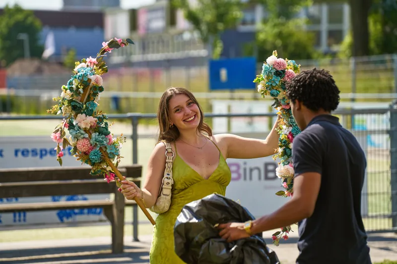 Een gast in een groene jurk lacht met twee bloemenbogen in haar handen