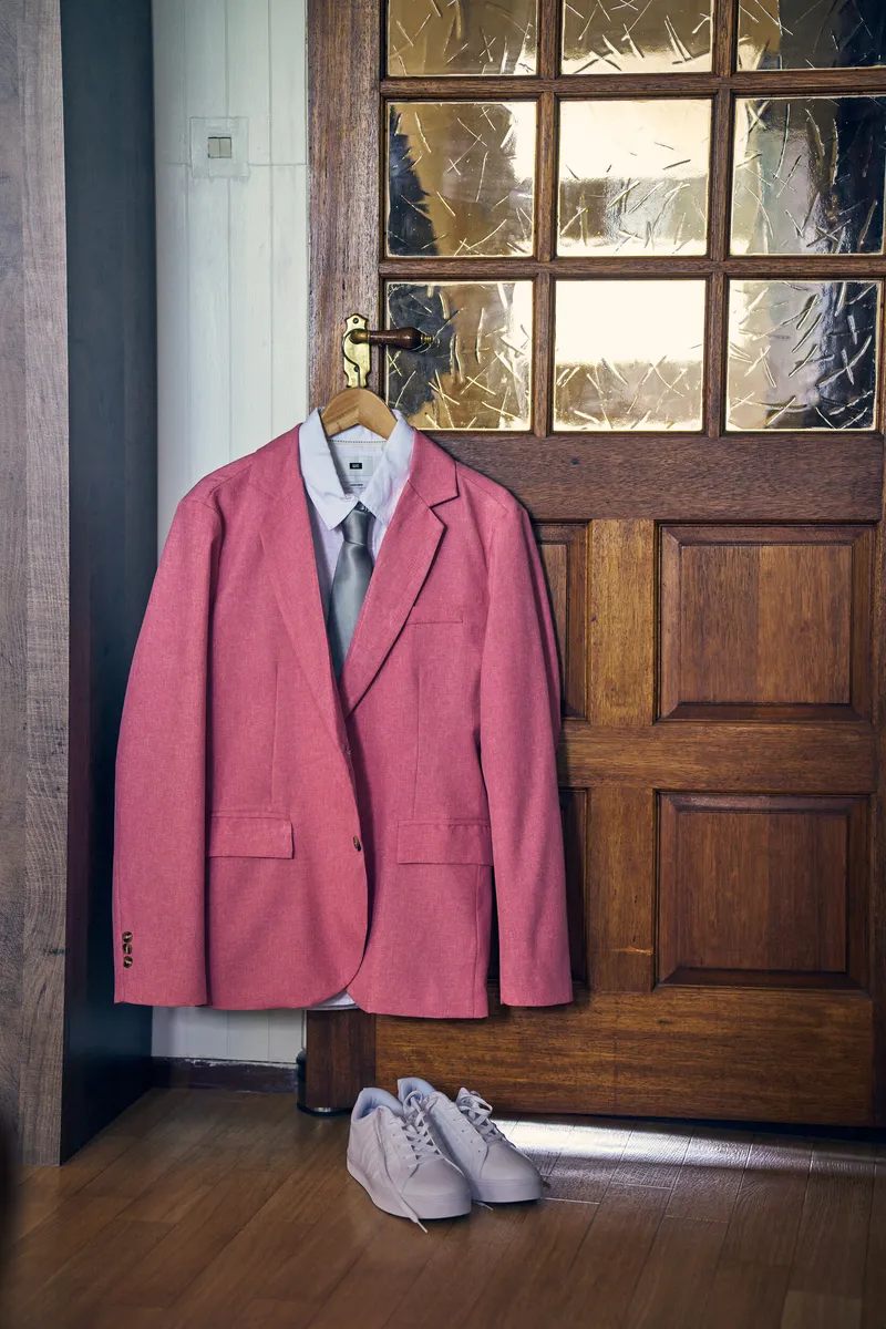 Het roze pak van Olav hangt aan een houten deur, de witte sneakers eronder