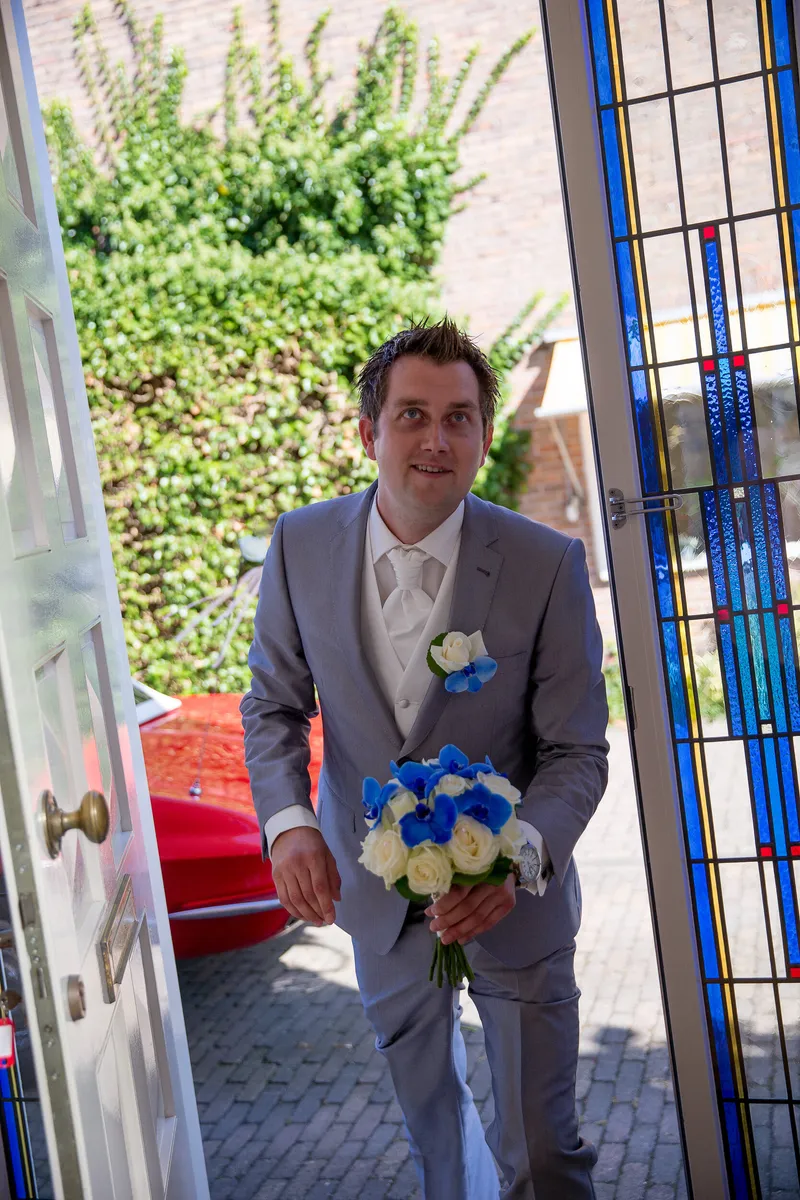 Ferry met het blauwe boeket bij de voordeur, de rode auto erachter