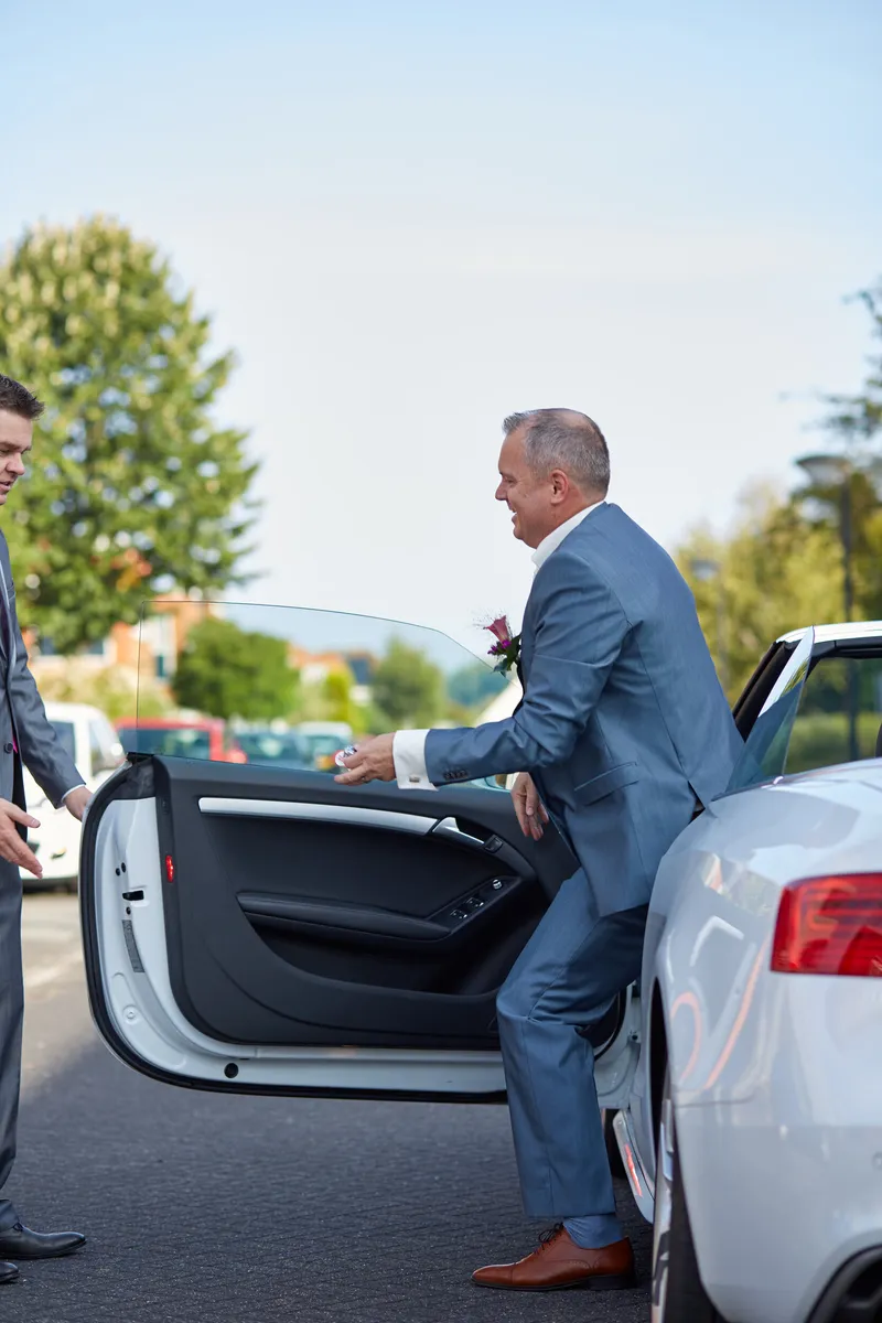Eric stapt in zijn blauwe pak uit de witte Audi