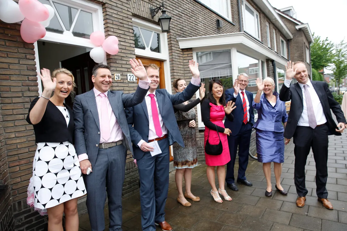 Familie en vrienden zwaaien met roze ballonnen voor het huis