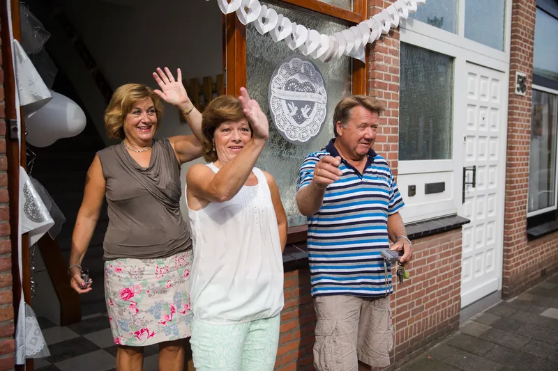 Familie en buren zwaaien het bruidspaar uit voor het huis