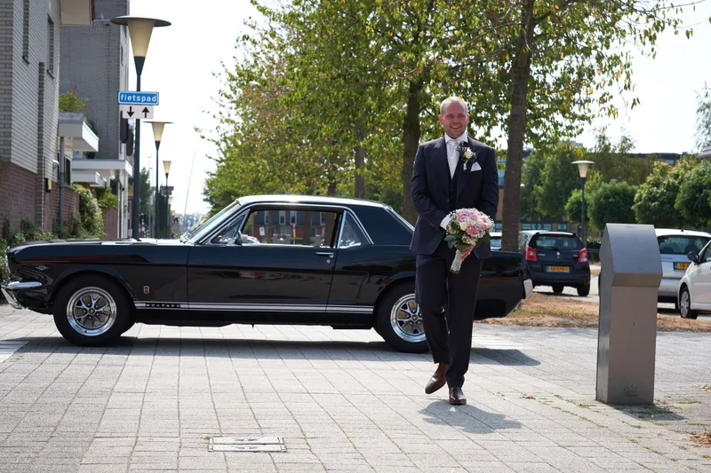 Kevin loopt met het boeket naar het huis, de zwarte Mustang op de achtergrond