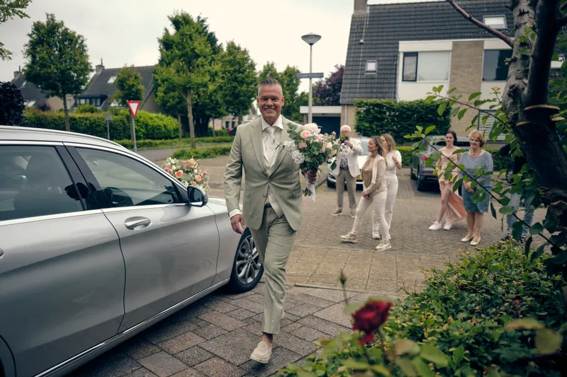 Marco loopt met het boeket naar de voordeur, langs de trouwauto
