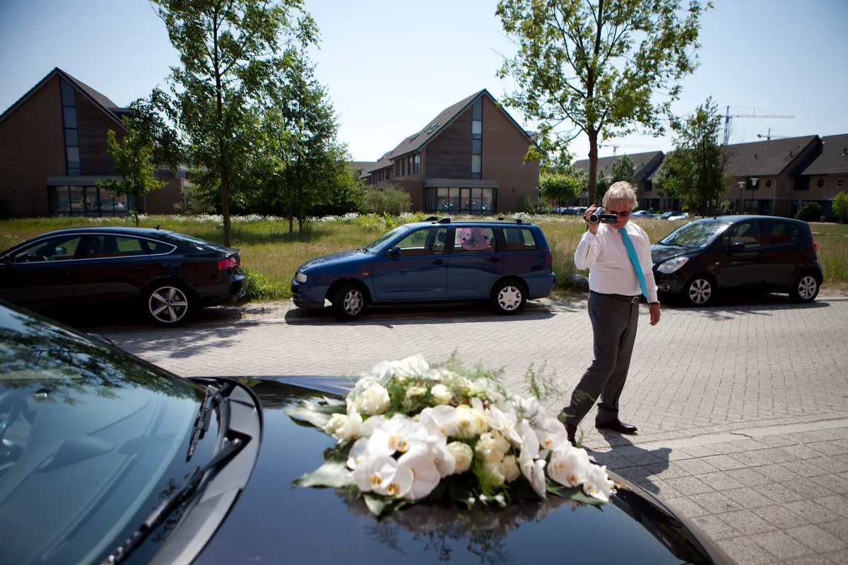 De trouwauto met bloemen op de motorkap, in een rustige woonstraat