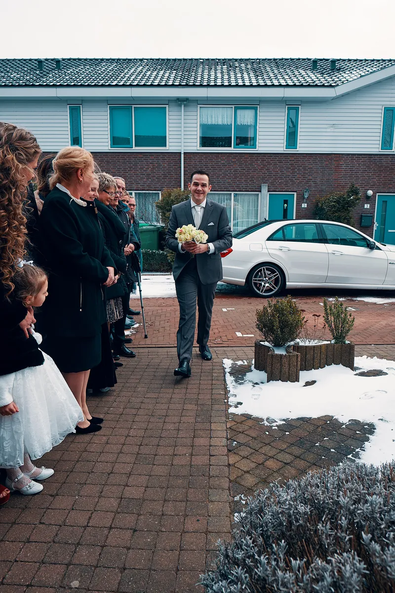 Maurice loopt met het boeket over het pad, de familie staat klaar in de sneeuw