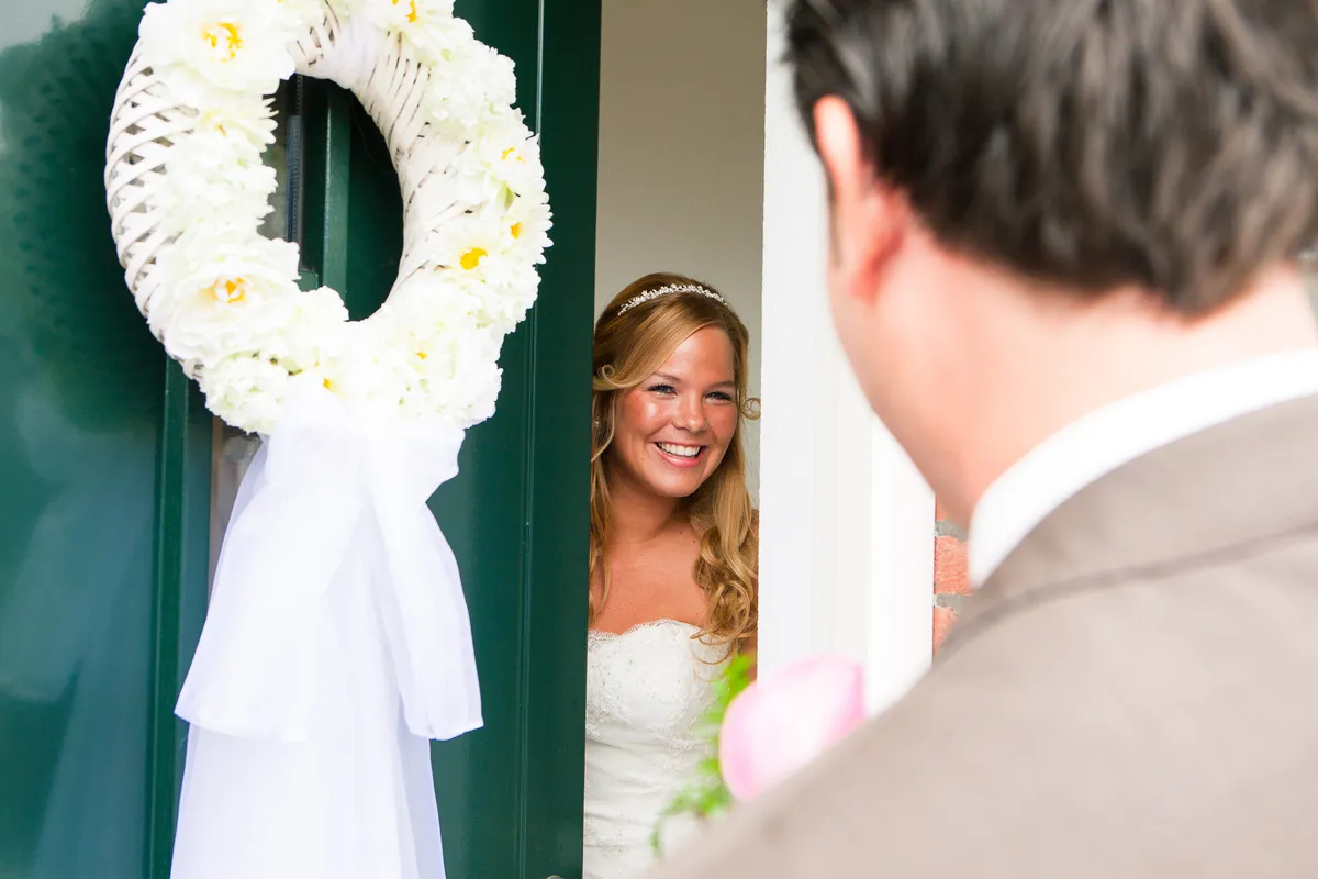 Esther kijkt om de voordeur met de witte krans naar Jan-Willem