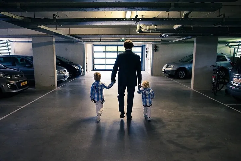 Een vader loopt met twee kleine jongens aan de hand door een parkeergarage