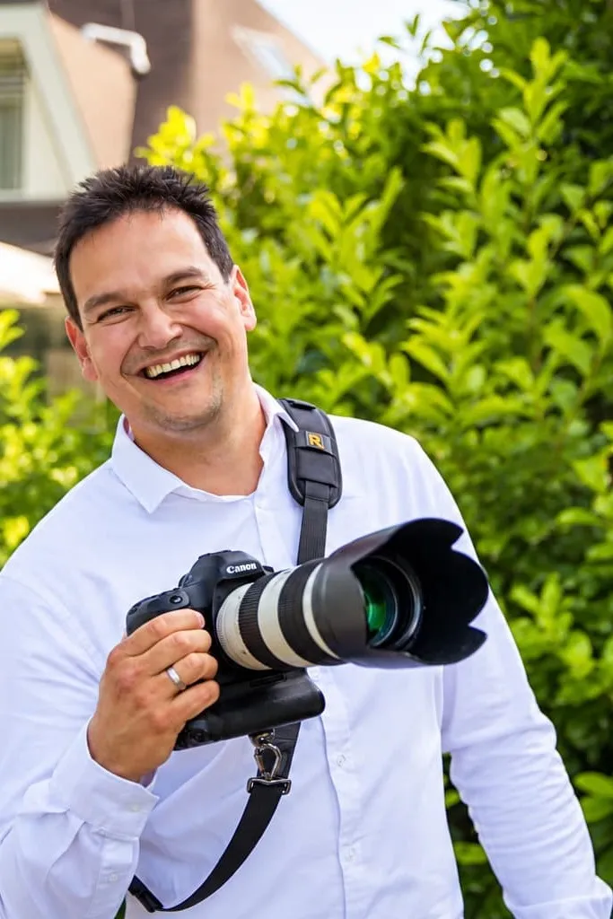 Stefan Segers lachend met zijn camera in een groene tuin