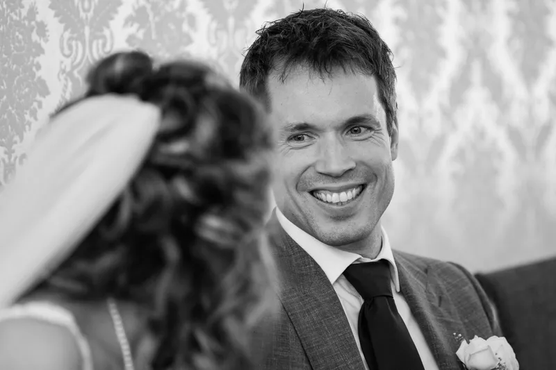 Joris lacht voor het behang van de trouwzaal, in zwart-wit