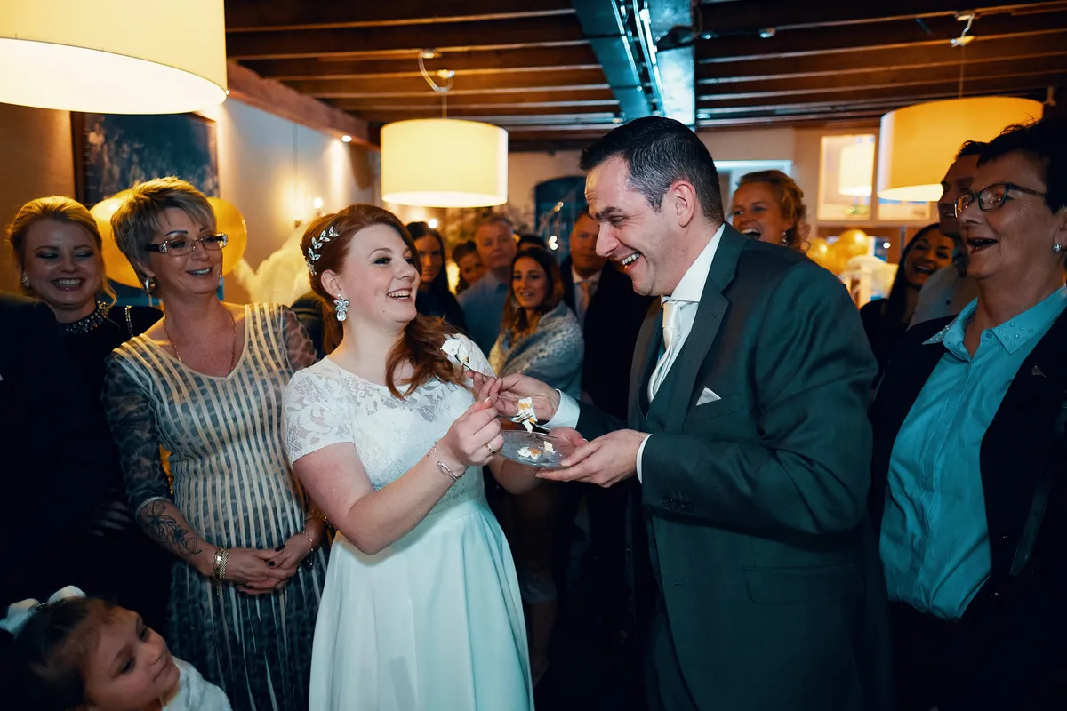Naomi en Maurice delen het eerste stuk taart, de gasten lachen mee