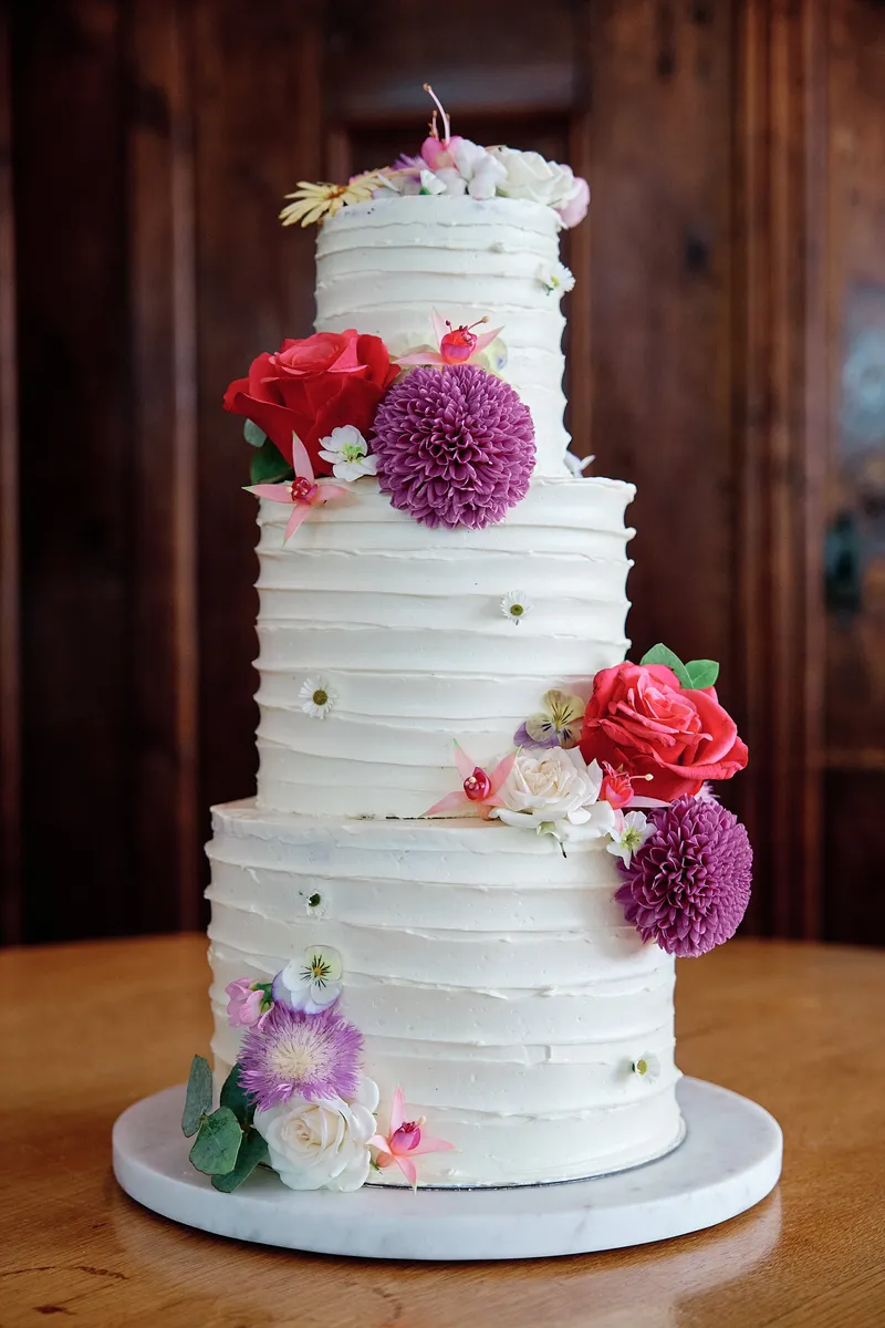 De witte bruidstaart van drie lagen met roze en paarse bloemen
