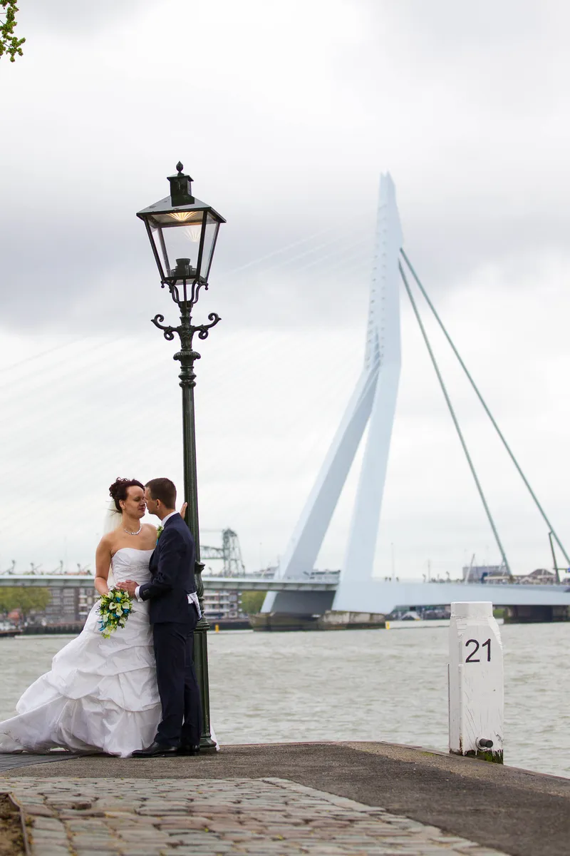 Anne en Hans bij een lantaarn, met de Erasmusbrug op de achtergrond