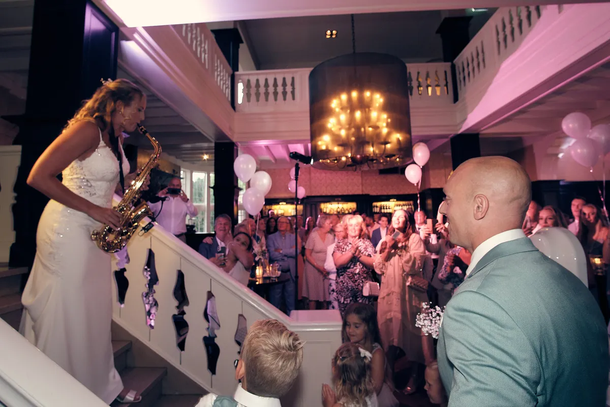 Kim speelt saxofoon bovenaan de trap, Dennis, de kinderen en de gasten kijken toe