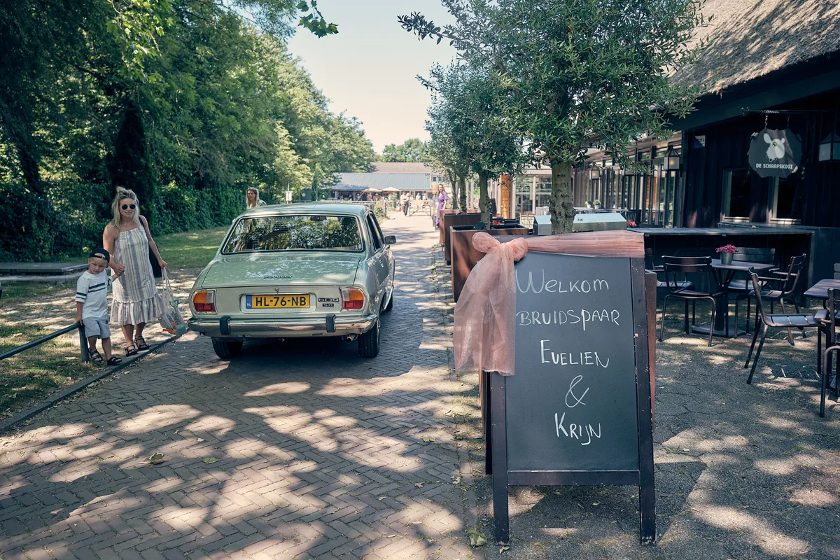 De witte Peugeot rijdt De Schaapskooi op, langs een krijtbord met hun namen