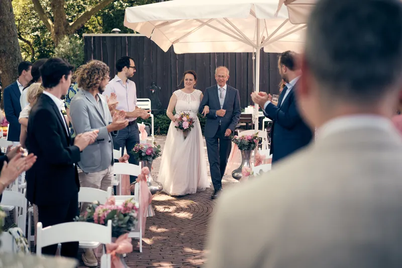 Evelien loopt aan de arm van haar vader naar Krijn, tussen de gasten door