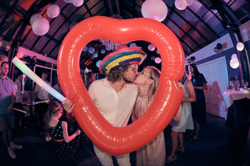 Twee gasten kussen door een opblaasbaar rood hart, een van hen met sombrero