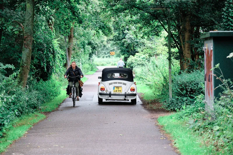De witte oldtimer rijdt over een smalle weg door het groen