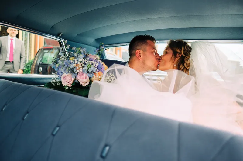 Lotte en Daniel kussen in de oldtimer, met bloemen op de achterbank