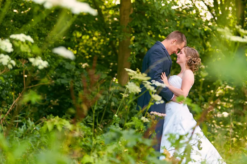 Linsey en Tim kussen tussen hoog groen met witte bloemen