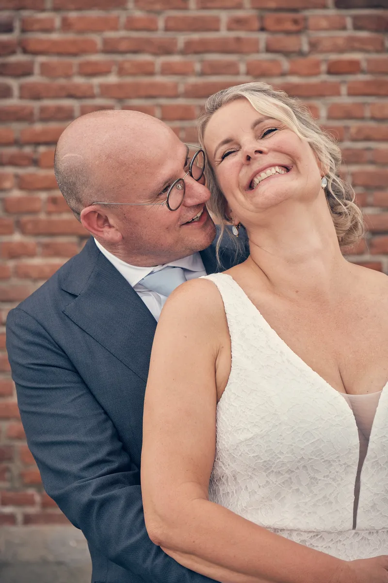 Bram omarmt Elles van achteren tegen de bakstenen muur