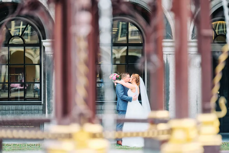 Een gouden paal op de voorgrond, Stefan en Victoria klein bij de Tweede Kamer