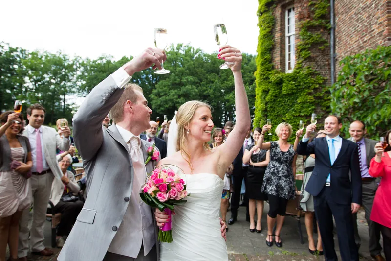 Loes en Jan heffen het glas, omringd door gasten in de tuin van het slot