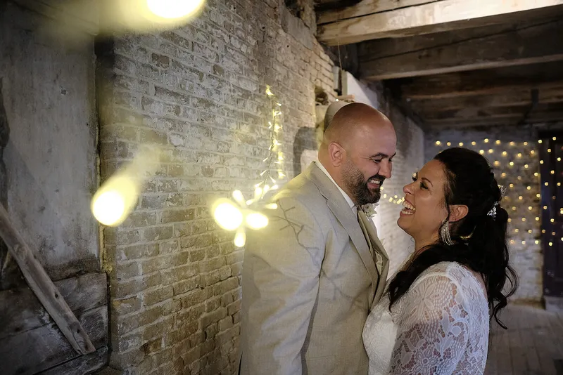 Regina en Michael lachen naar elkaar bij een oude bakstenen muur met lampjes